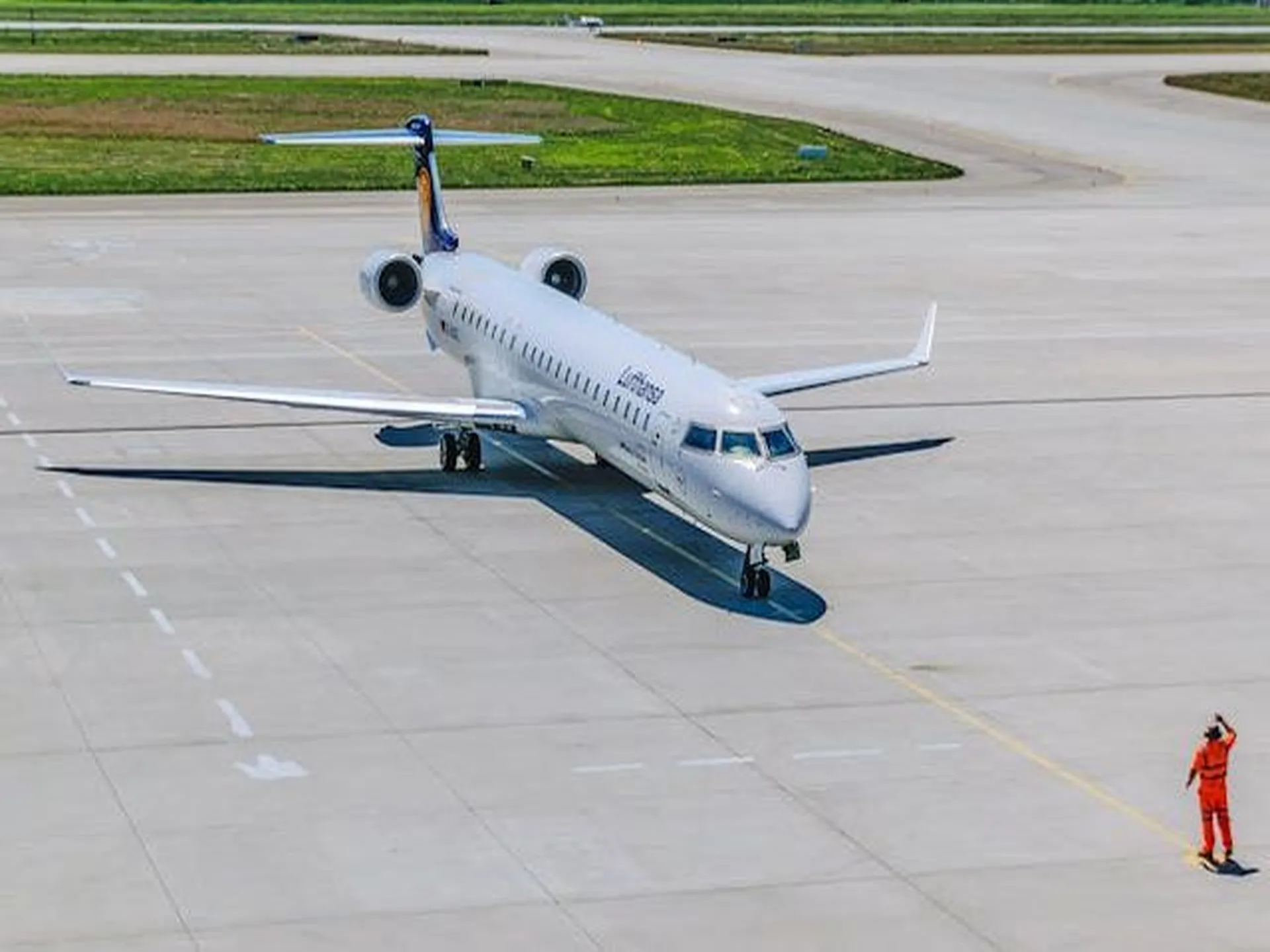An image of a passenger jet on the tarmac and an airport worker meeting the plane
